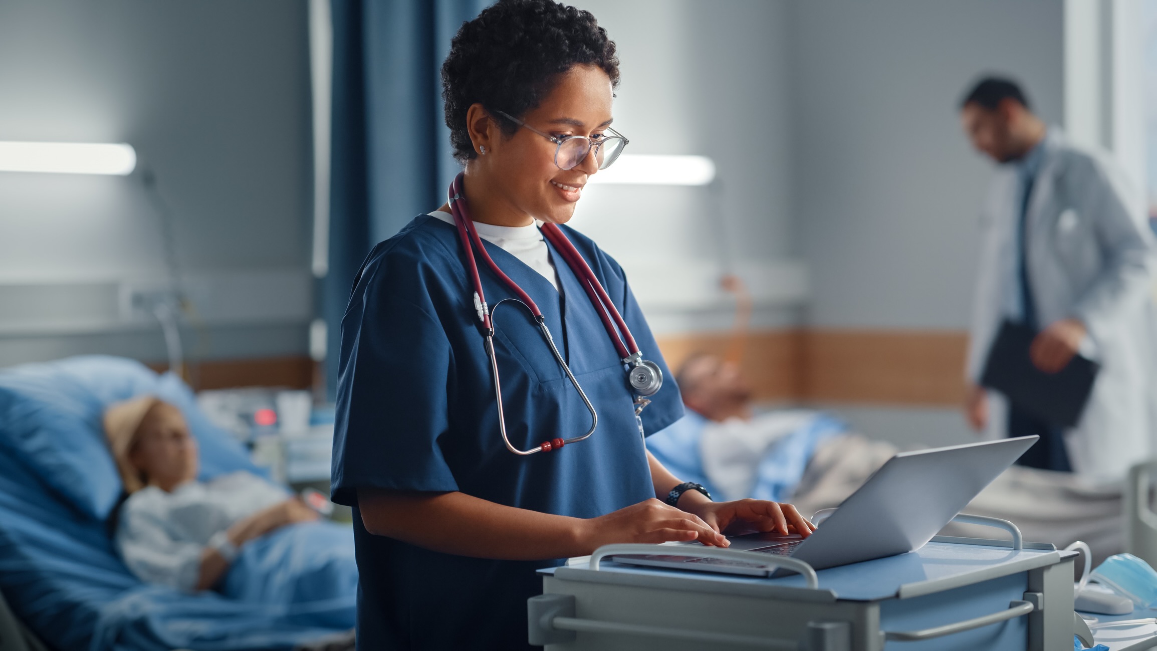 Hospital Ward: Professional Smiling Black Female Head Nurse or Doctor Wearing Stethoscope Uses Medical Computer. In the Background Patients in Beds Recovering Successfully after Sickness and Surgery