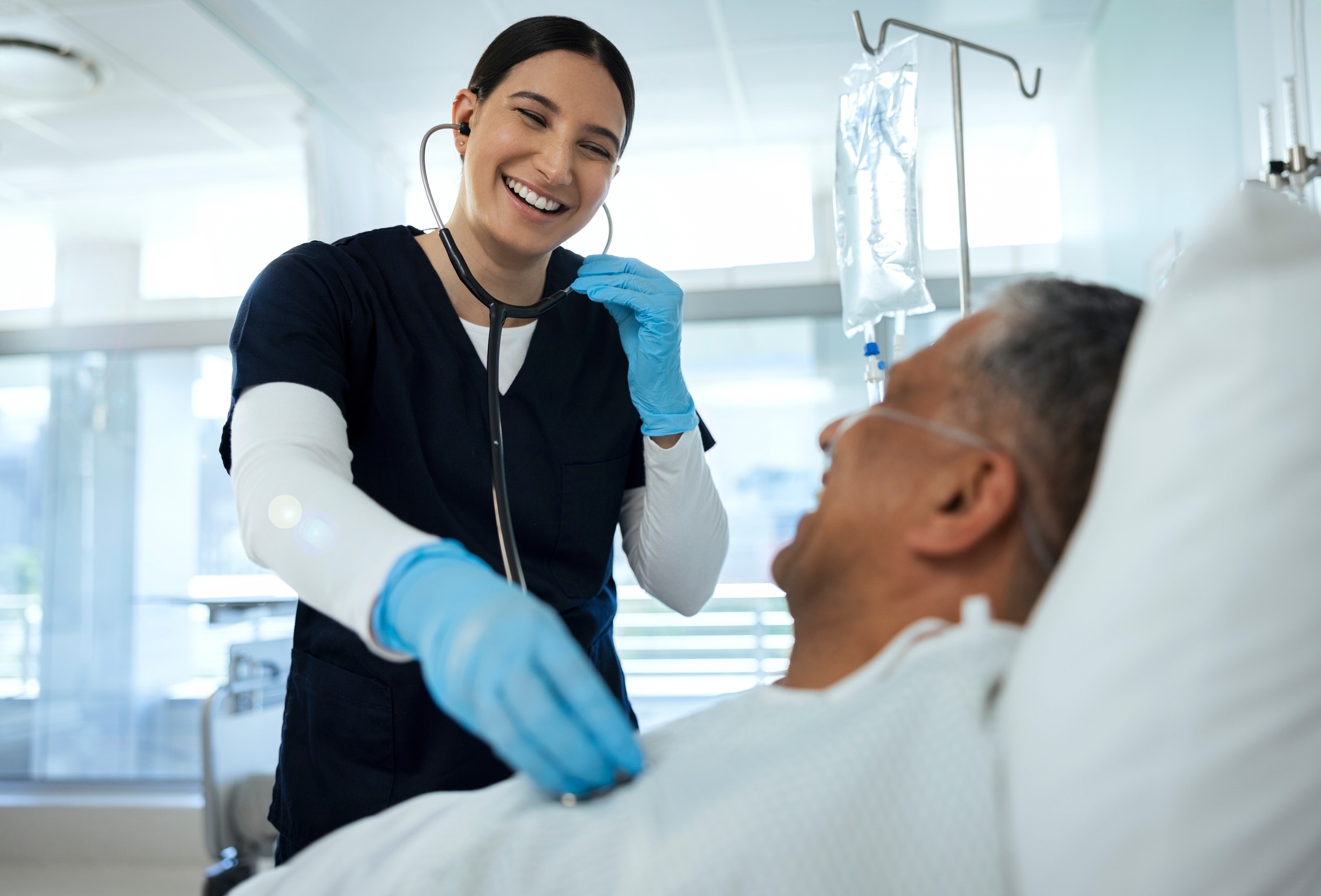 Happy woman, nurse and checking patient heart rate, beat or monitoring in healthcare, recovery or checkup on bed at hospital. Female person or medical employee helping elderly man for exam at clinic